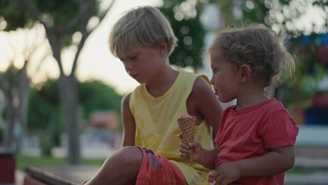 Little brother share ice cream with elder brother at a park. Cute little boy share ice cream with his brother
