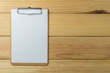 Blank wooden clipboard with paper on wood background copy space. Business, office supply, stationery concept.