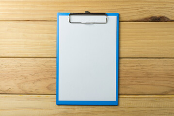 Blank blue clipboard with paper on wood background copy space. Business, office supply, stationery concept.  