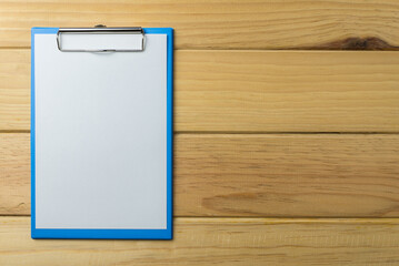 Blank blue clipboard with paper on wood background copy space. Business, office supply, stationery concept.