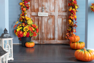 Fototapeta na wymiar Cozy wooden porch of house with pumpkin in fall. Halloween composition design home with yellow fall leaves and flowers. House entrance staircase decorated for autumn holidays, fall flowers and pumpkin