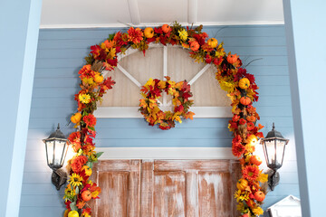 Entrance of house door decorated with autumn leaves for holiday. Fall yellow garland with leaves and pumpkins, fall decor. Halloween design home. Street lanterns on Entrance home	