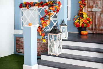 House entrance staircase decorated for autumn holidays, fall flowers and pumpkins. Cozy porch of the house with wooden lanterns in fall time. Halloween design home with yellow fall leaves and lamps	