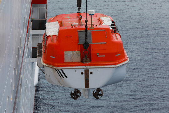 Lowering orange totally enclosed lifeboat to water. Abandon ship drill. Lifeboat training. Man over board drill.