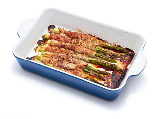ceramic baking dish with aspargus covered with bacon isolated on white background