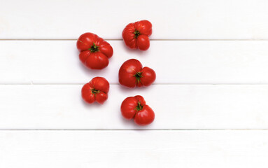 Red ripe tomatoes lie on a white wooden background.
