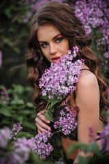 a beautiful girl with makeup and hair styling in underwear stands in a garden with lilacs on a summer evening
