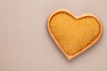 Brown sugar in heart wooden bowl shape on pasttel background.