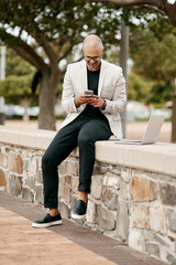 Obraz premium Stylish, cool smiling businessman on a phone in the park outside in nature. Happy man texting, chatting or reading social media messages on a smartphone outdoors on a break from work with copy space