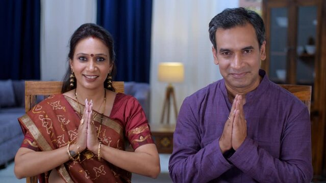 A middle-aged Indian husband-wife doing a Namaste gesture - greeting  respect  traditional way  posing for camera . A happy Gujarati couple - togetherness and bonding  quality time  small nuclear f...