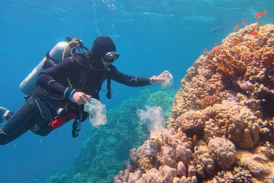 Man scuba diver cleaning plastic  from the tropical coral reef. World ocean contaminated by plastic.