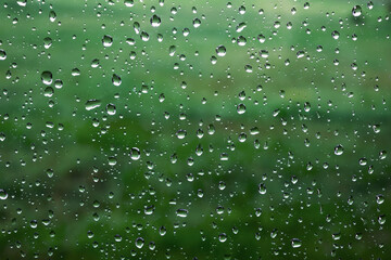Close-up of rain drops on a window pane. Gloomy damp rainy weather. Green color background. Concepts of sad or depressed mood. Autumn season wallpaper. Abstract texture. Blurred garden. Wet season