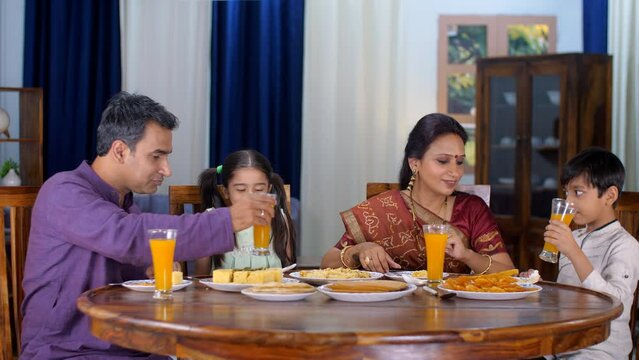 A happy Gujarati family - husband wife and young kids having food  family time  small nuclear family  mealtime. A small Indian family having their lunch together - traditional dress  Indian sibling...