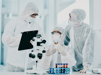 Science and medical research doctors working on covid vaccine test while wearing protective hazmat suits in modern medicine laboratory. Group of healthcare scientists discussing blood treatment