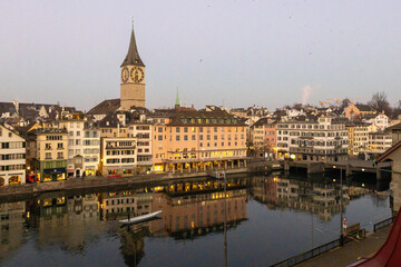 Fototapeta na wymiar Blick auf den Fluss Limmat in Zürich, früher Morgen, rotes Licht, Spiegelungen im Wasser, ein Boot in der Stille des Morgens