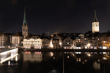 Fototapeta na wymiar Altstadt von Zürich über der Limmat, Nacht, die Kirchen Fraumünster und St. Peter, Spiegelung im Wasser, helle Lichter