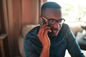Young student talking on a phone call to a friend, colleague or family member. Black male university or college learner studying design, marketing or architecture sitting and chatting at home