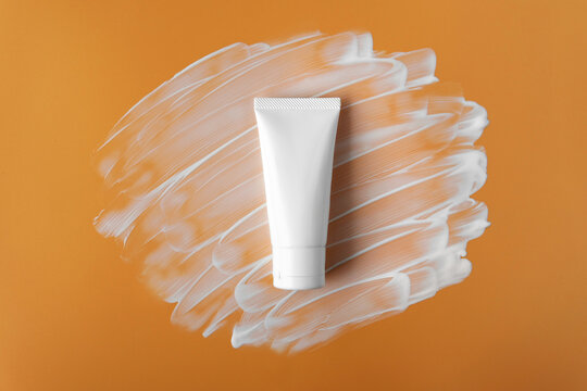 Mockup Facial Skincare White Tube Bottle With Blank Label And White Color Tint Uv Sunscreen With SPF 50+ PA+ Or 30 Reef Safe Ingredient Smear On Soft Plain Solid Orange Isolated Background.