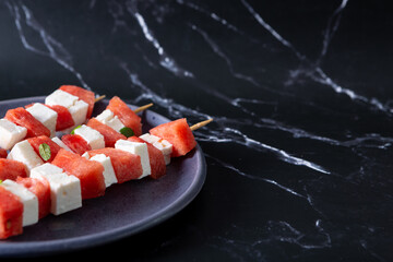 Watermelon and cheese skewers with mint leaves on a black background