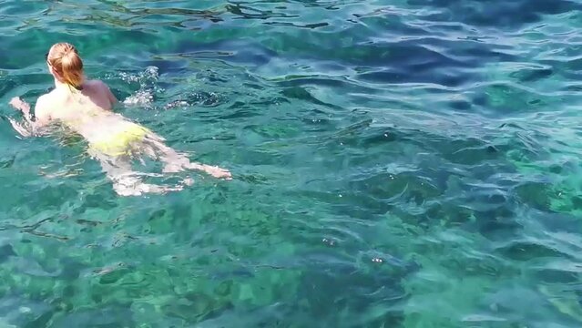 Girl in a bikini swims in crystal clear water in a transparent sea. A woman swims in turquoise water. Crystal clear water surface. Summer lifestyle. The Aegean sea. Turkey, Kusadasi.