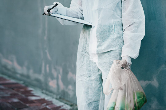 Forensic investigator collecting evidence on a murder scene on a street holding a plastic bag and wearing a hazmat suit. Crime researcher doing a scientific criminal investigation outdoors in a city
