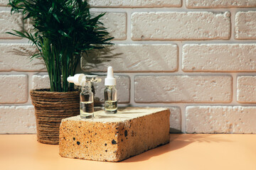 A group of transparent bottles on brown brick with face care products. Serum in a glass package with green palm on background. Front view