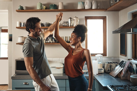 Happy, in love and dancing while an interracial couple have fun and enjoying time together in home kitchen. Husband and wife sharing a dance while being active and affectionate in loving relationship