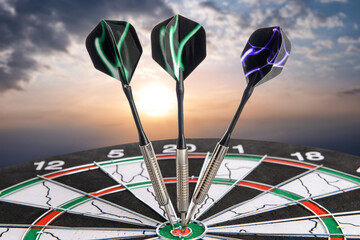 Board with darts against cloudy sky at sunrise, closeup
