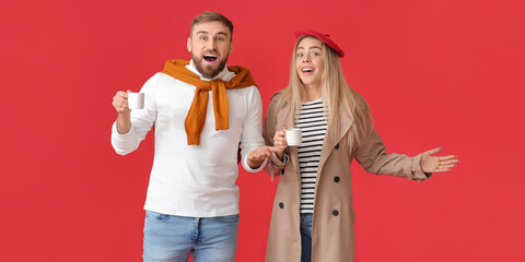 Surprised young couple with cups of hot coffee on red background
