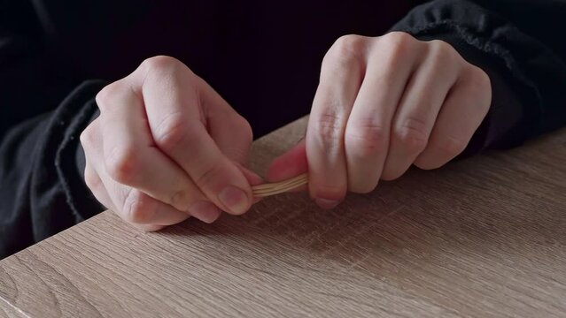 close-up of a woman in a black jacket angry and breaking wooden toothpicks with her fingers against the background of a wooden table