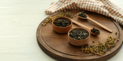 Bowls with dry tea leaves and chamomile on table