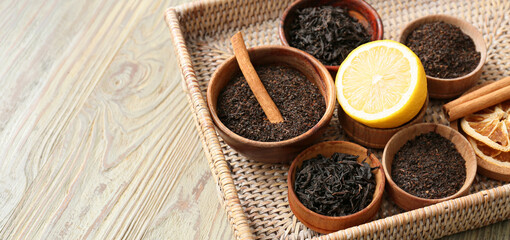 Bowls with dry tea leaves, cinnamon and lemon on wooden background