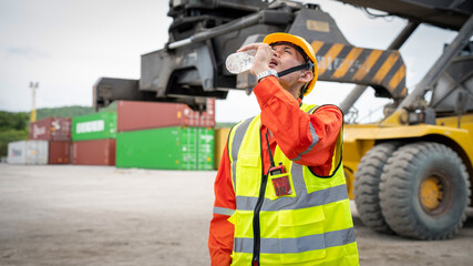 Foreman or worker is drinking a bottle of water after finishing work and relaxing on the old truck at cargo container port