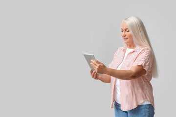 Mature woman using tablet computer for navigation on light background