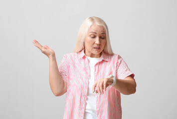 Confused mature woman with smartwatch for navigation on light background