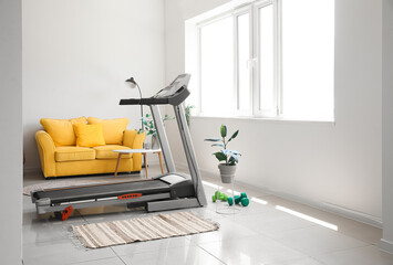 Interior of light living room with treadmill and yellow sofa