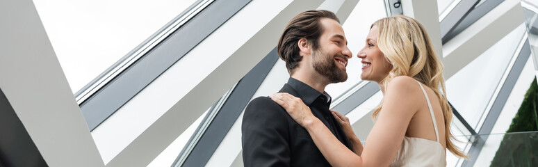 Low angle view of elegant couple smiling at each other while hugging in restaurant, banner.