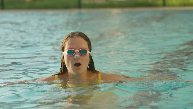 A girl in a yellow swimsuit, pink swimming glasses, puts on a nose clip and dives under the water. close-up, slow motion