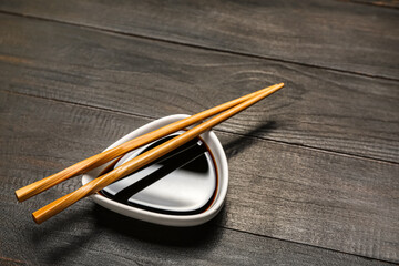 Bowl of soy sauce and chopsticks on dark wooden background