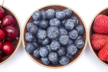 Blueberries, strawberries and cherry in bowls on white background. Top view