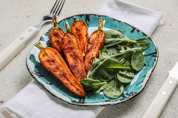 Plate of tasty baked carrots and spinach on light background, closeup