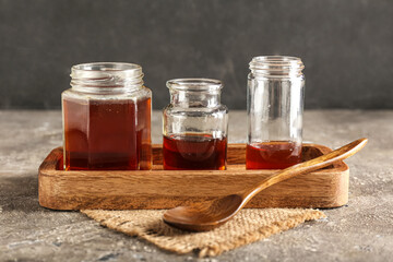Wooden board with jars of tasty maple syrup on table