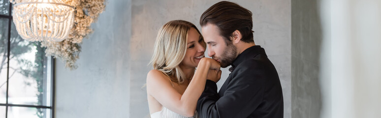 Bearded man in suit kissing hand of smiling girlfriend in restaurant, banner.