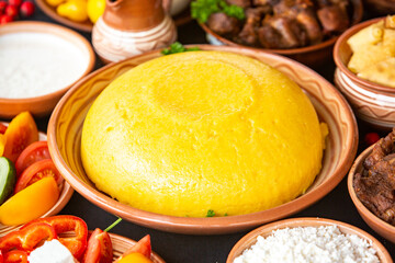 Homemade Romanian Food with polenta, meat, cheese and vegetables. Delicious corn porridge in clay dishes. Mamaliga or polenta, a traditional dish in Moldova, Hungary and Ukrainian cuisine.
