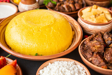Homemade Romanian Food with polenta, meat, cheese and vegetables. Delicious corn porridge in clay dishes. Mamaliga or polenta, a traditional dish in Moldova, Hungary and Ukrainian cuisine.

