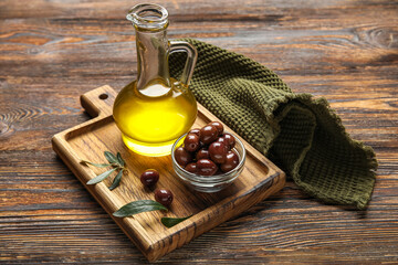 Board with decanter of oil and olives on wooden background