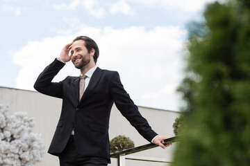 Low angle view of positive groom touching hair on terrace of restaurant.