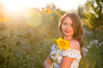 Fototapeta premium a young woman with a sunflower in a field at sunset. copy space. Enjoying the little things. spends time in nature in summer
