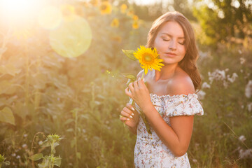 a young woman with a sunflower in a field at sunset. copy space. Enjoying the little things. spends time in nature in summer