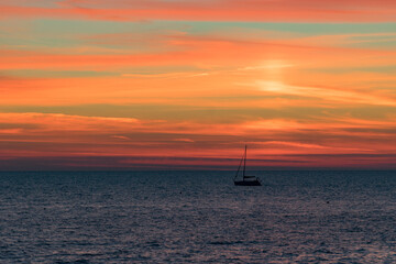 Seascape with a vibrant sunset over a calm sea and a floating boat.